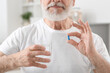 Senior man with glass of water and pill at home, closeup