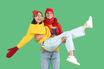 Wall Mural - Happy young couple in warm clothes having fun on green background