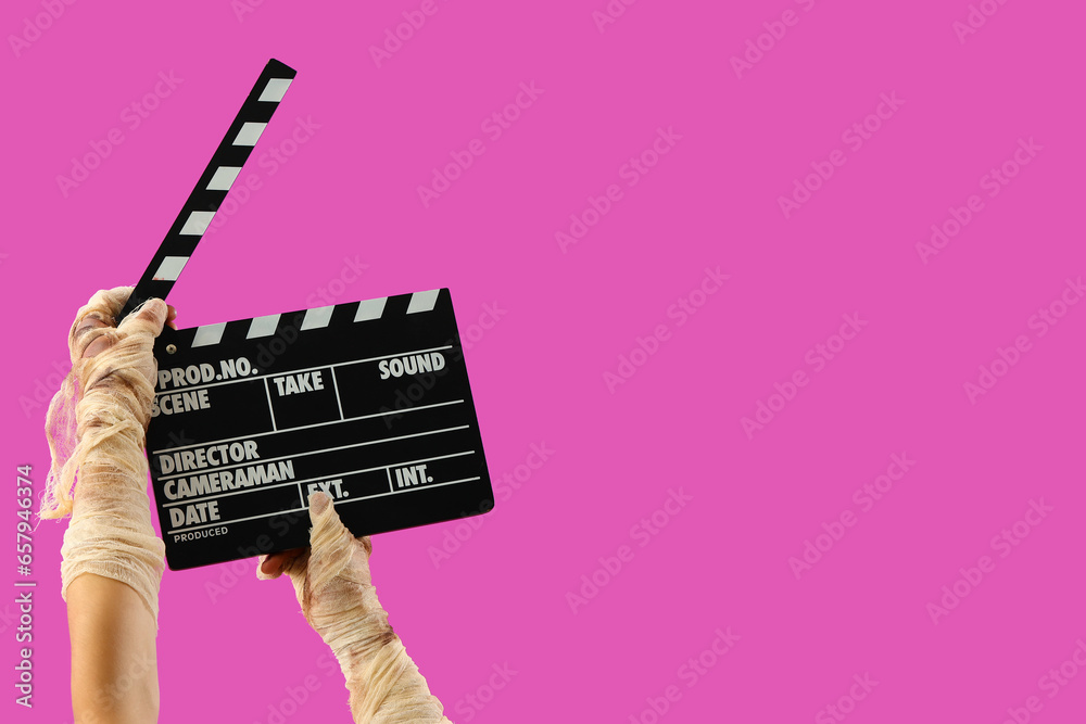 Mummy hands with cinema clapperboard on pink background. Halloween celebration