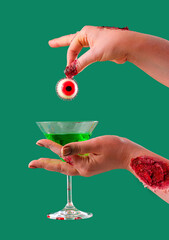 Zombie hands with cocktail and eyeball on green background. Halloween celebration