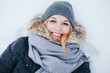 A portrait of a beautiful young blonde woman lying on the snow smiling to the camera on a cold winter day