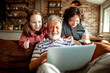 © Marko Geber - Grandfather and grandchildren online shopping from a laptop on the couch at home