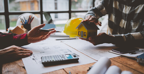 Two young Asian businessmen or architects are describing architectural house model in their office together for the construction of housing estate project in prime location the location is perfect