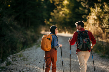 Rear view of the adventurous couple embarks on a mountain trail adventure, fully equipped with hiking gear, in the heart of a lush forest