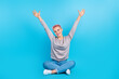 © deagreez - Full length photo of overjoyed cheerful person sit floor crossed legs raise arms isolated on blue color background