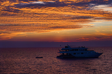 Beautiful wide twilight sunset evening sky reflect on sea water with silhouette boat in ocean and epic cloud pattern background landscape with love, peace and loneliness mood vibes on vacation trip.