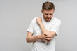 Man touching hand elbow feeling pain isolated on gray background after injury. Neuralgia, pinched nerve in arm after injury, broken fracture bruised hand. Health problems, bad symptom, hurt concept.