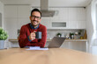 © Moon Safari - Portrait of smiling businessman holding coffee cup while sitting by laptop at desk in home office