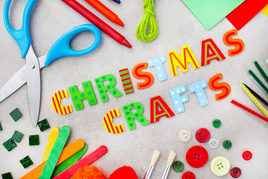 Christmas crafts in bright lettering with colorful craft supplies on a mottled grey surface