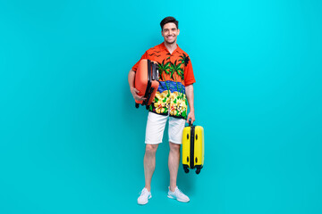 Sticker - Full size photo of friendly optimistic guy wear tropical shirt stylish shorts hold luggage at airport isolated on blue color background