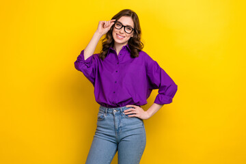 Poster - Portrait of smart positive girl with wavy hairstyle wear violet blouse fingers touching glasses arm on waist isolated on yellow background