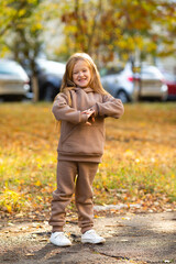 Wall Mural - Happy little child girl laughing and playing in the autumn on the nature walk over fallen leaves outdoors. Autumn season. Happy child over nature background at city street.