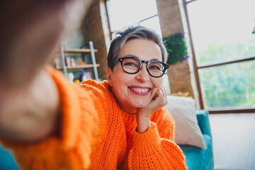 Canvas Print - Photo of dreamy pretty elderly lady wear orange pullover spectacles arm hand cheek recording video indoors apartment room