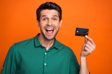 Poster - Portrait of funny young guy hold plastic card payment with no commission shopaholic advertisement nfc isolated on orange color background