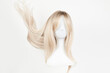 © amixstudio - Natural looking blonde wig on white mannequin head. Long hair on the plastic wig holder isolated on white background, front view.