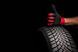 Fototapeta Dmuchawce - Car tire service and hands of mechanic holding new tyre on black background with copy space for text
