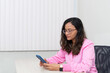 © Thales - Portrait of a psychopedagogue, wearing pink clothes, in her office, sitting, looking at the appointments scheduled on her cell phone. Helps with school performance.