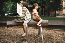Playful Boys Sitting On Outdoor Play Equipment In Park
