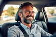 Mid adult man smiling while driving car and looking at mirror for reverse. Happy man feeling comfortable sitting on driver seat in his new car. Smiling mature businessman with seat belt on driving.