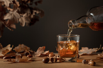 Poster - Whiskey with ice on a wooden table with dried-up oak leaves.