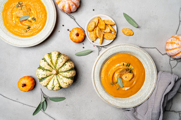 Wall Mural - Pumpkin soup and organic pumpkins, top view, gray background. Seasonal autumn food - Spicy pumpkin soup with cream, croutons and pumpkin seeds.