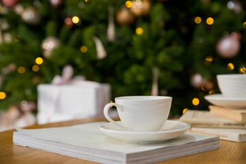 Cup of black coffee on wooden table in cafe. Christmas lights and gold garland on background. Atmospheric winter hygge. Warm cup of coffee on background of christmas tree with lights. Cozy home