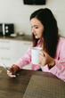© Mila - A young girl with black hair in a pink shirt sits at a table with a phone and a white mug in a cozy room with brown brick. Woman working, talking on the phone, drinking coffee in a modern cafe.Morning