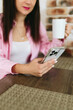 © Mila - A young girl with black hair in a pink shirt sits at a table with a phone and a white mug in a cozy room with brown brick. Woman working, talking on the phone, drinking coffee in a modern cafe.Morning