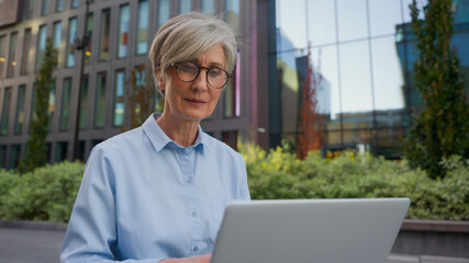 Caucasian middle aged mature woman senior old businesswoman office manager architect developer business lady working online in city typing on laptop computer outdoors busy female employer work distant