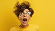 Portrait of excited young woman wearing eyeglasses with flying hair surprised on yellow background.