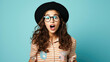 Young beautiful woman, fashion teen girl student wearing glasses and hat standing over blue background surprised and shocked with surprise expression, excited face