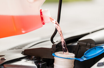 Close-up service worker man driver pouring red non freezing windshield cleaning glass washer fluid in hood car tank from canister bottle. Summer or winter fluid windscreen liquid glass window cleaner