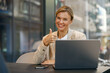 © Yaroslav Astakhov - Businesswoman with laptop is sitting on modern office background and showing thumb up