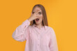 Embarrassed woman covering face with hand on orange background