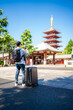 Back view of unrecognizable Hispanic traveler man in casual clothes with backpack standing while taking picture of historic Senso-ji temple in Asakusa Tokyo on sunny day, Japan