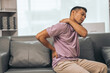 © NanSan - Middle-aged Asian Indian man suffering from back pain, spine and neck pain. sitting on the sofa