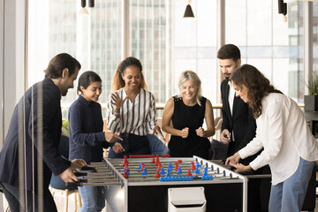 Poster - Happy diverse team of business friends meeting at funny board game in office lobby, modern co-working, laughing, shouting, giving support to excited table soccer players