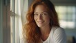 © Restyler - Beautiful happy ginger woman in loose home clothes at the window. Portrait of a smiling lady. Feminine beauty.