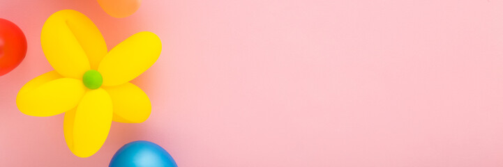 Wall Mural - Colorful balloons and beautiful flower head created from yellow balloon on pink table background. Pastel color. Wide banner. Closeup. Making different shapes. Empty place for text. Top down view.