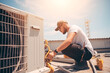Technician working on air conditioning outdoor unit on hot sunny day. HVAC worker professional occupation