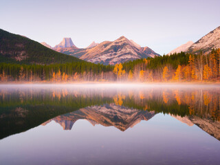 Wall Mural - Lake and mountains in a valley at dawn. Reflections on the surface of the lake. Mountain landscape at sunrise. Foggy morning. Natural landscape with bright sunshine.