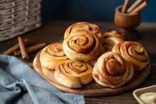 Homemade Fresh Baked Cinnamon Rolls On A Wooden Board With Cinnamon Sticks, Sugar And Napkin Wooden And Dark Background