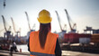 © Mosaic Media - A female civil engineer examines drawings at a container terminal in the harbor, seen from behind, with a blurred backdrop.