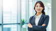 © BlazingDesigns - Cheerful asian business woman standing in office with arms crossed.