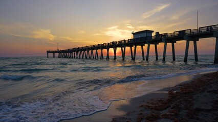 Sticker - Idyllic sunset over sandy beach at Venice fishing pier in Florida. Evening seascape with surf waves crashing on sea shore covered with sargassum seaweed