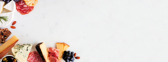 Aufkleber - Selection of charcuterie cheeses, meats and appetizers. Above view corner border on a white marble background with copy space.