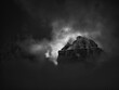 The peak of a rocky mountain in the dark illuminated by sunlight through the clouds in black and white, Dolomites, Italy