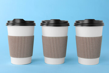 Wall Mural - Paper cups with black lids on light blue background. Coffee to go