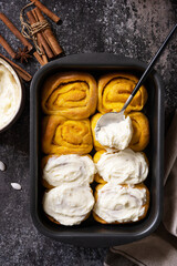 Canvas Print - Homemade seasonal autumn homemade pastry. Freshly baked pumpkin cinnamon rolls or cinnabon with cream cheese on a dark stone background. View from above.