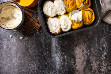 Canvas Print - Freshly baked pumpkin cinnamon rolls or cinnabon with cream cheese on a dark stone background. Homemade seasonal autumn homemade pastry. View from above. Copy space.
